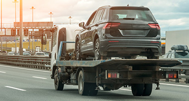 a tow truck transporting a black broken down car down a motorway
