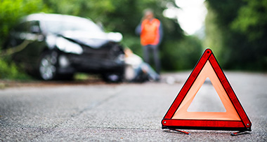 A close up of a red emergency triangle on the road with a car accident in the background