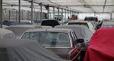 multiple cars stored under a roof, some of which with coverings over them